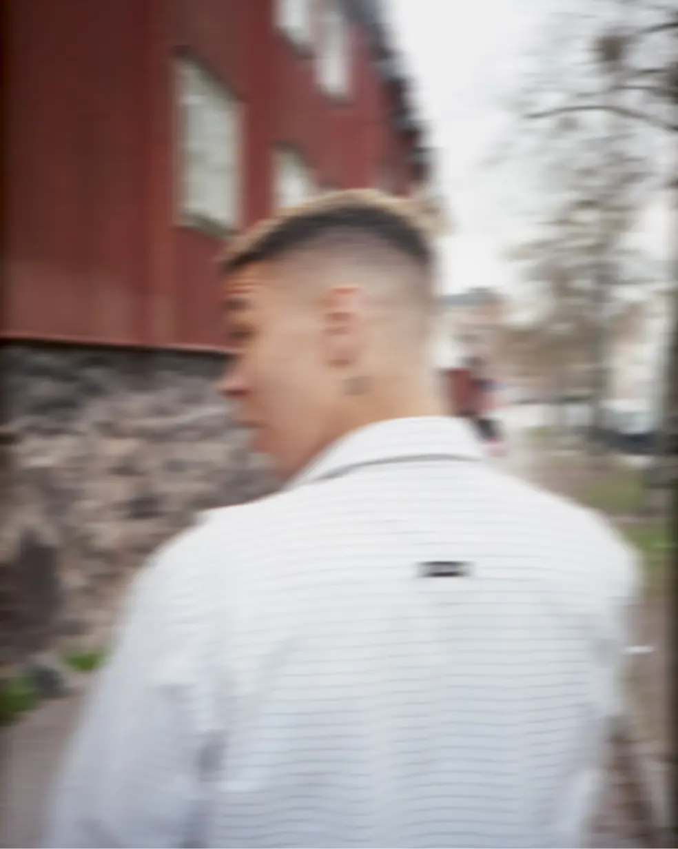 A blurred image of a person walking with their back to the camera, wearing white clothing. The person's head is tilted back.